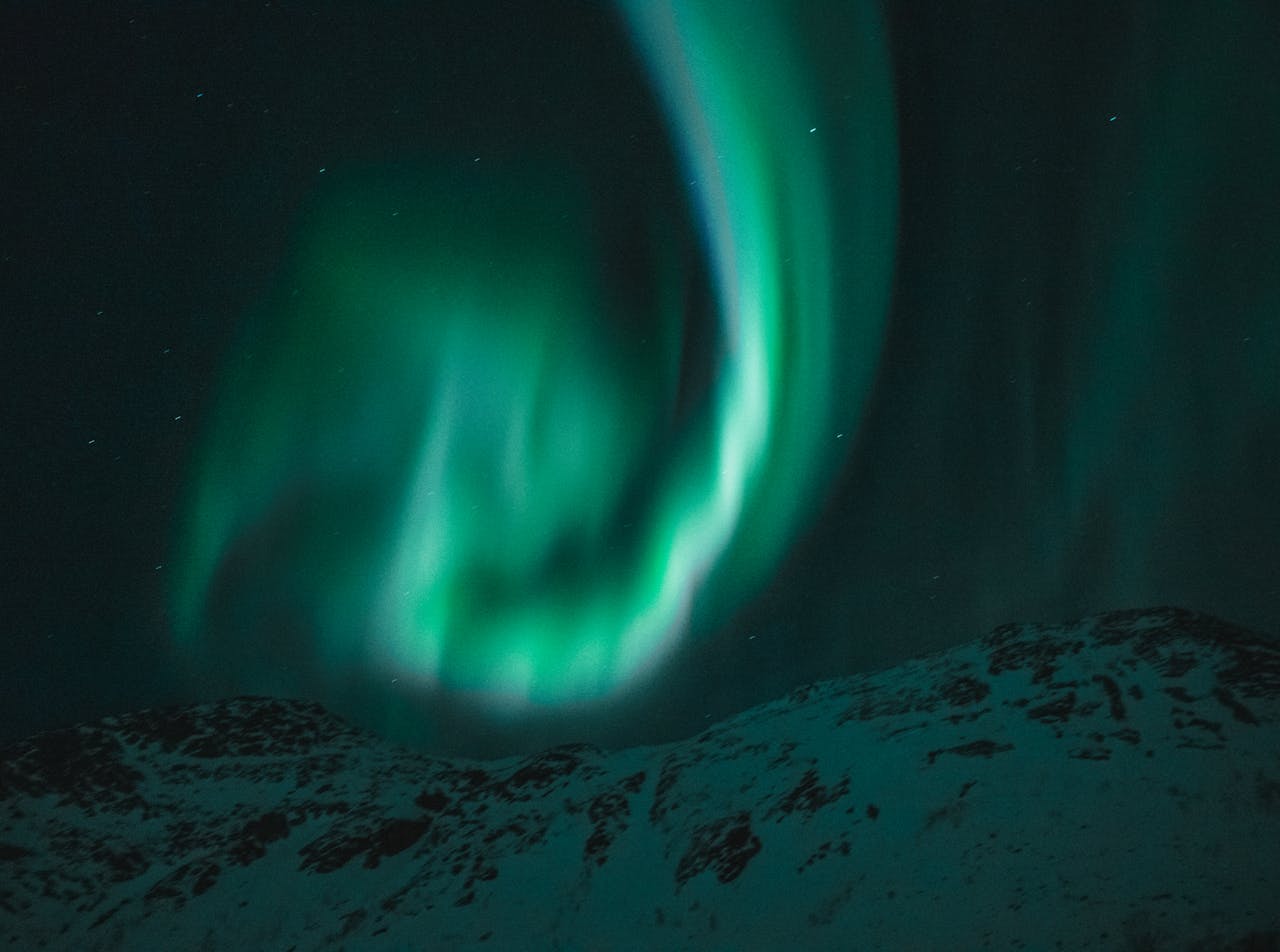 services-04 Beautiful aurora borealis illuminating the night sky over snow-covered mountains under a starry sky.